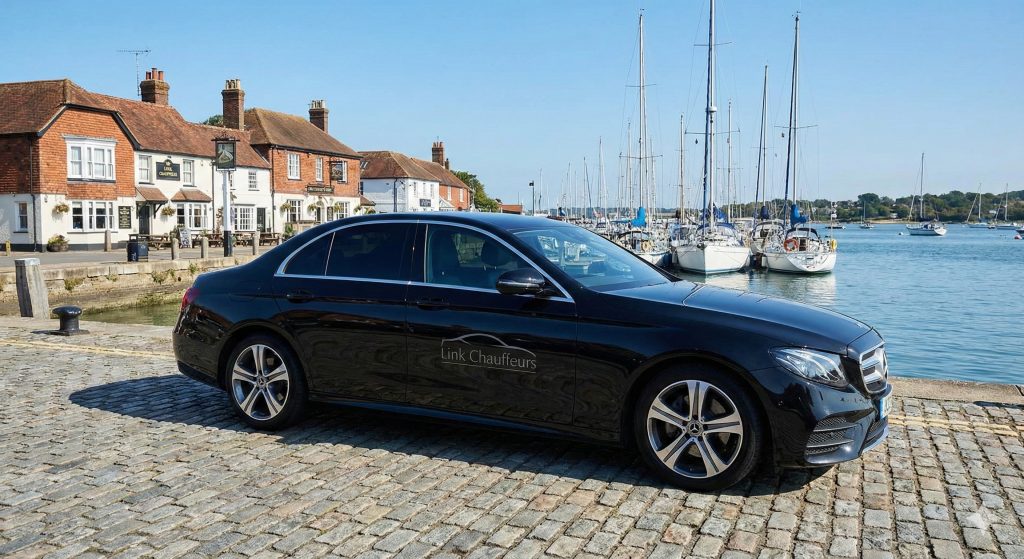 Premium Mercedes chauffeur car parked on the quay in Hamble-le-Rice with yachts and riverside pubs in the background.